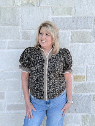 Woman wearing a leopard print shirt and blue jeans standing against a stone wall.