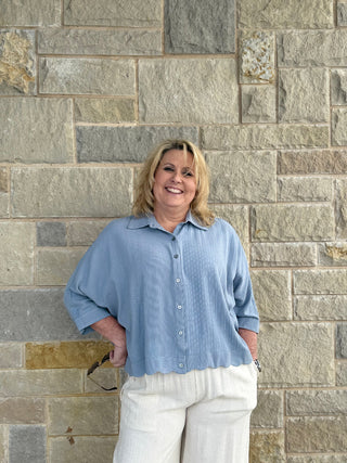 Woman wearing a blue shirt and white pants standing against a stone wall.