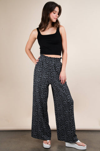 Woman wearing a black sleeveless top and patterned wide-leg pants against a beige background