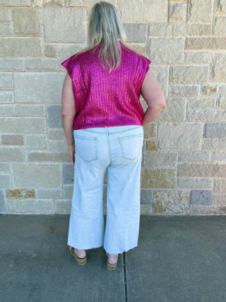 Person wearing a pink sleeveless top and white pants standing against a brick wall.