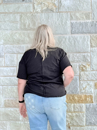 Person wearing a black shirt and light blue jeans standing against a stone wall.