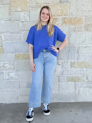 Woman wearing a blue shirt and light blue jeans standing against a stone wall.