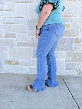 Person wearing blue jeans and a green top against a gray brick wall.