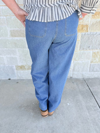 Person wearing blue jeans and a striped shirt against a stone wall.