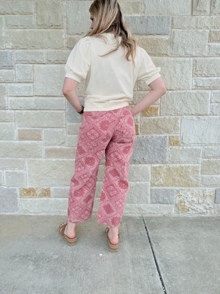 Person wearing a white top and pink patterned pants standing against a stone wall.