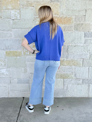 Person wearing a blue sweater and light blue jeans standing against a stone wall.