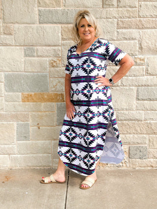 Woman wearing a patterned dress standing against a stone wall.