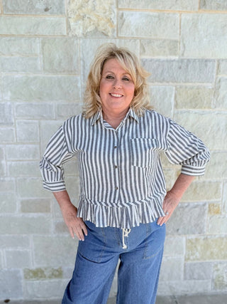 Woman wearing a striped shirt and jeans standing against a stone wall.