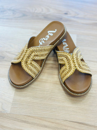 Gold sandals with woven design on a wooden floor
