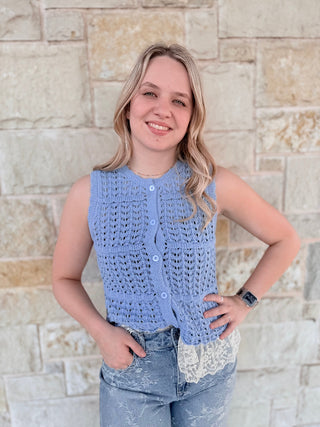 Woman wearing a blue sleeveless crochet top against a stone wall.