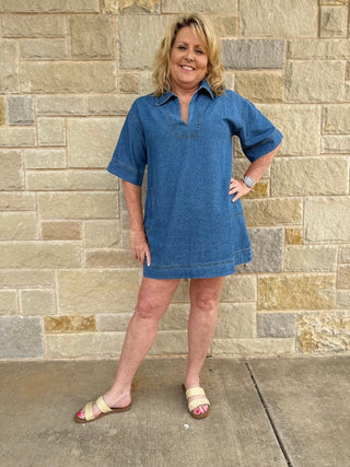 Woman wearing a blue dress standing against a stone wall.