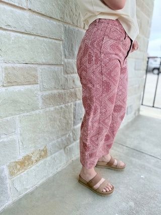Person wearing pink patterned pants and sandals standing against a light stone wall.