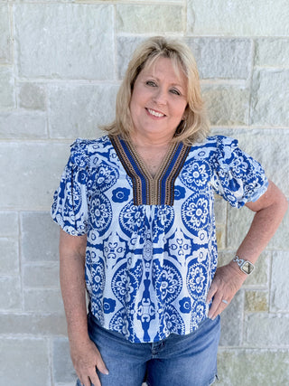 Woman wearing a blue and white patterned top against a stone wall.