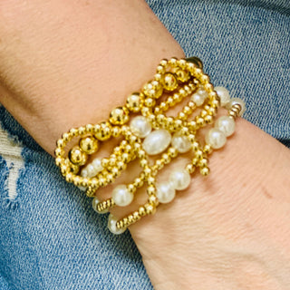 A bracelet with a gold bow design and white pearl-like beads displayed on a person's wrist.