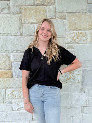 Woman wearing a black top and light blue jeans standing against a stone wall.