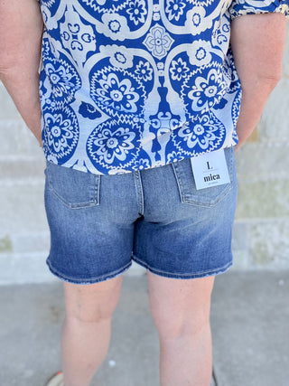 Person wearing a blue and white patterned shirt and denim shorts with a visible brand tag.