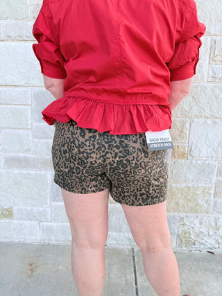 Person wearing a red jacket and leopard print shorts against a light stone wall.