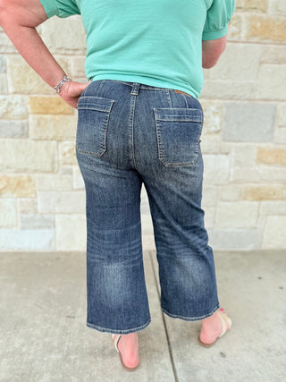 Person wearing blue jeans and a green shirt against a stone wall.