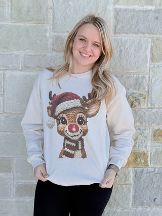 Woman wearing a sweater with a reindeer design against a stone wall.