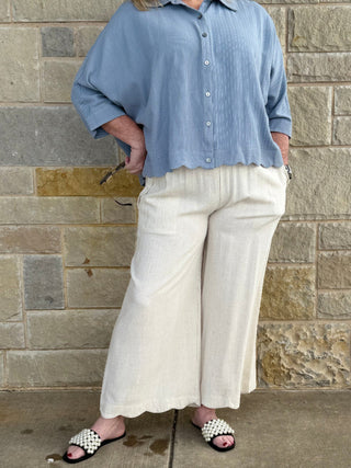 Person wearing a blue shirt and white pants standing against a stone wall.
