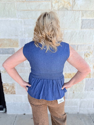 Person wearing a blue sleeveless top with a peplum waist against a stone wall.