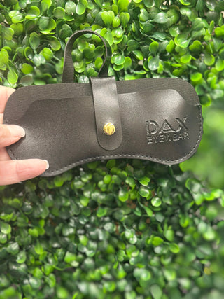 Black leather case with 'DAX EYEWEAR' branding held against a green leafy background