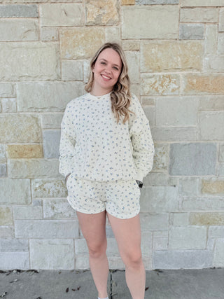 Woman wearing a white floral outfit standing against a stone wall.