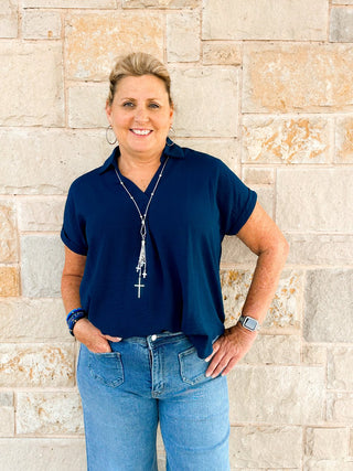 Woman wearing a navy blue shirt and blue jeans standing against a stone wall.