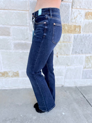 Person wearing blue flared jeans standing against a tiled wall.