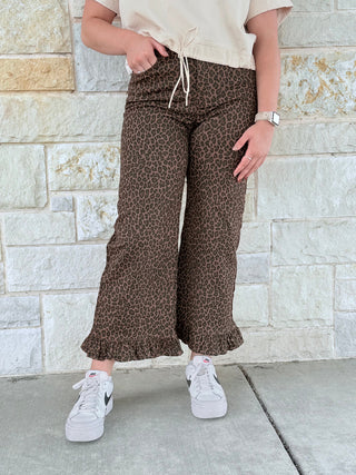 Person wearing leopard print pants and white sneakers against a stone wall.