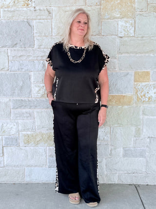 Woman wearing a black outfit with leopard print details against a stone wall.