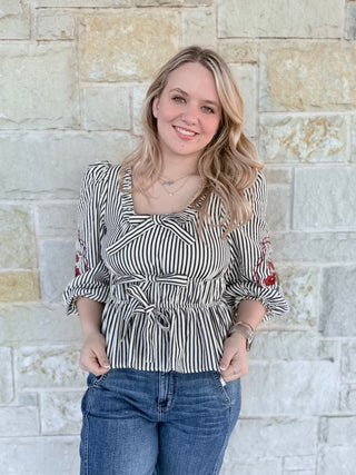 Woman wearing a striped top and jeans standing against a stone wall.