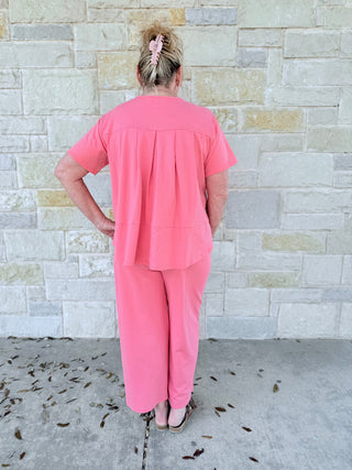 Person wearing a pink outfit standing against a stone wall.