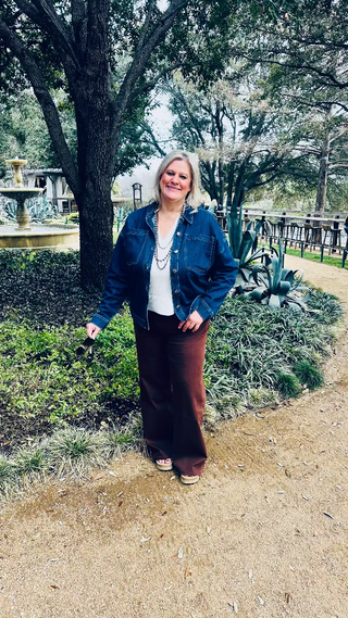 Woman standing outdoors in a garden with trees and a fountain in the background