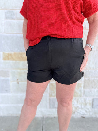 Person wearing black shorts and a red top against a textured wall.