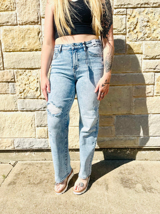 Person wearing light blue jeans and a black top against a stone wall.