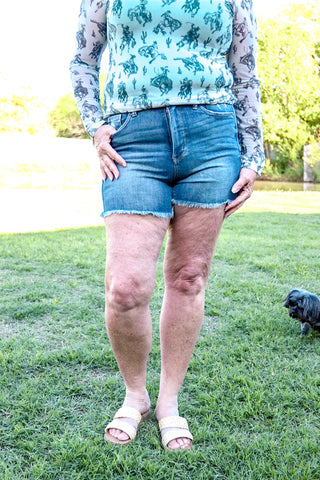 A person standing in a grassy area wearing high-waisted shorts with a fray hem design.