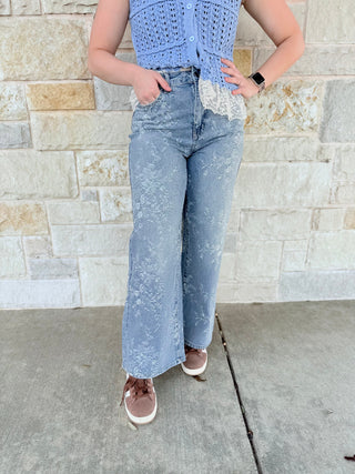 Person wearing a blue distressed jeans and a light blue top against a stone wall.