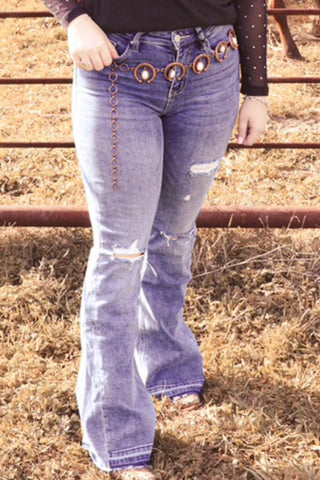 A person wearing high-rise flare jeans with a side panel design, standing in a field with a metal fence in the background.