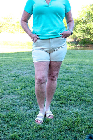 A person standing in a field wearing high waisted beige shorts and a green top with pockets.