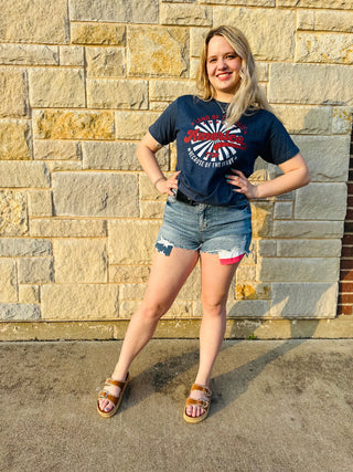 Woman wearing a blue t-shirt with a graphic design and denim shorts standing against a stone wall.