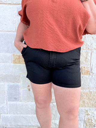 Person wearing a coral shirt and black shorts standing against a light stone wall.