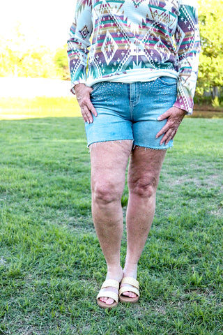 A person wearing high waisted blue denim shorts with rhinestone embellishments and a colorful, patterned top.
