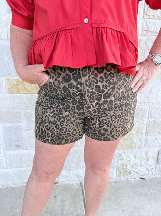 Person wearing a red top and leopard print shorts against a stone wall background