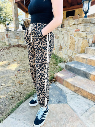 Person wearing leopard print pants with white stripes outdoors on a stone path.