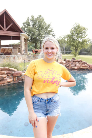 Person wearing a yellow 'Lake vibes' shirt by a pool