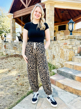Woman wearing a black top and leopard print pants standing outdoors.