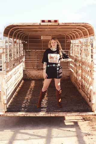 A person standing in the bed of a truck wearing a black t-shirt with a graphic of a cowgirl and a horse.
