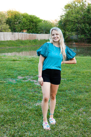 Woman in a blue top and black shorts standing on grass with trees in the background