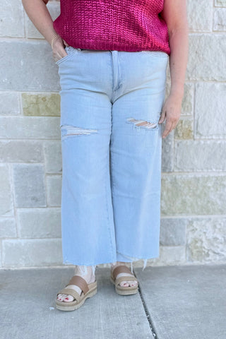 Person wearing light blue jeans with distressed details against a stone wall.